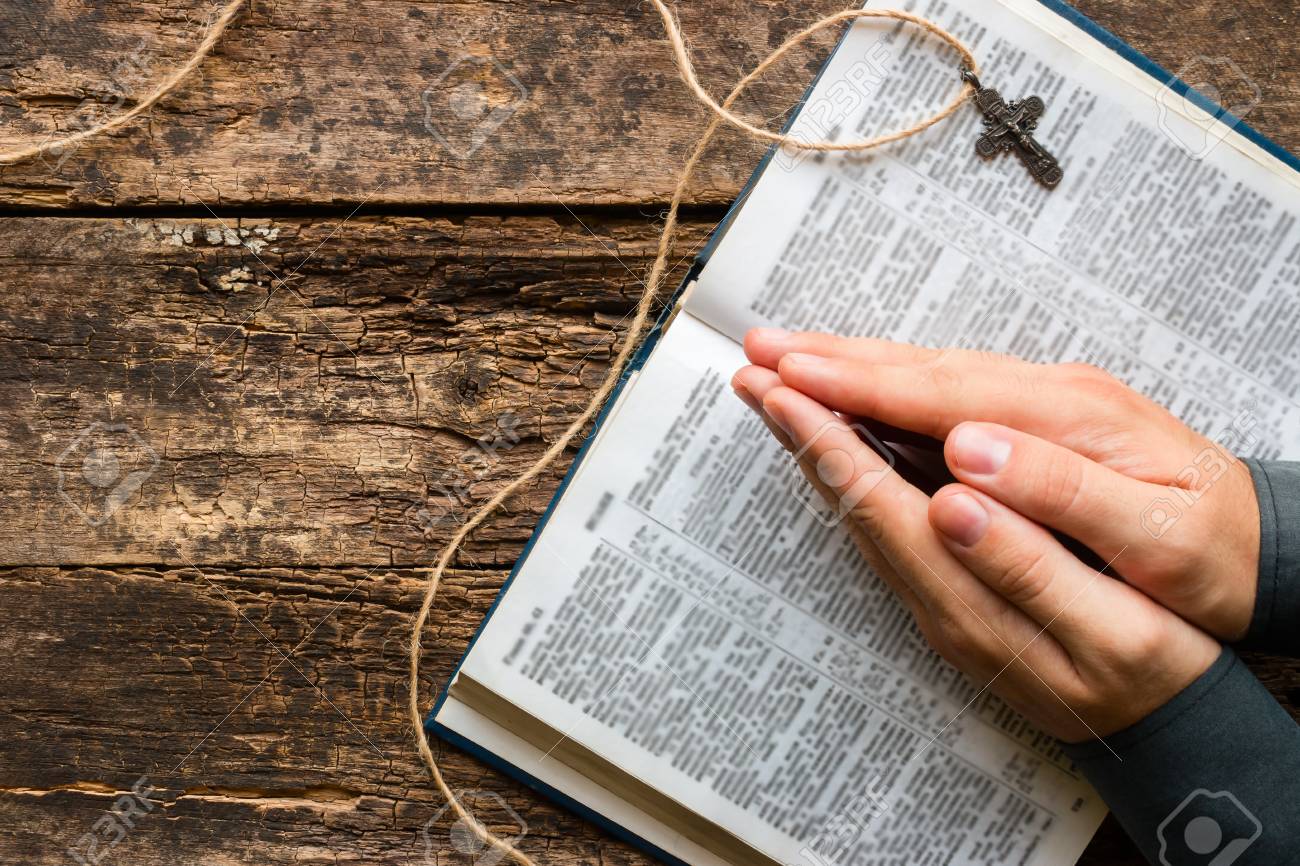 man reads a prayer from the Bible on the wooden background with space for text