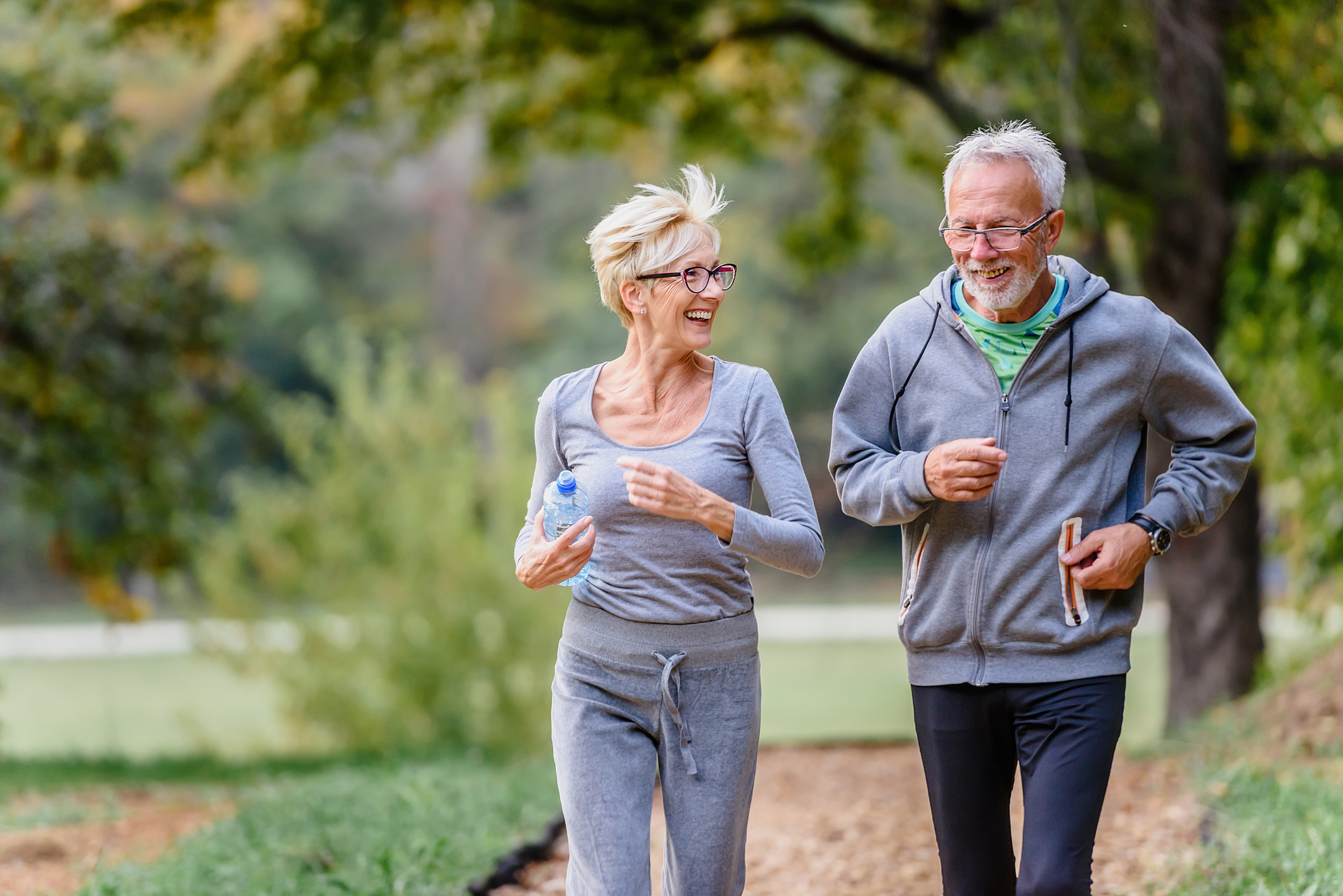 Cheerful active senior couple jogging in the park in the morning